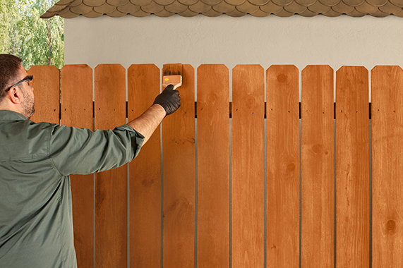 Man using a brush to apply Thompson’s WaterSeal Semi-Transparent Wood Protector in Natural Cedar to a backyard fence
