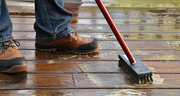 Someone using scrub brush to prepare deck for waterproofing. 