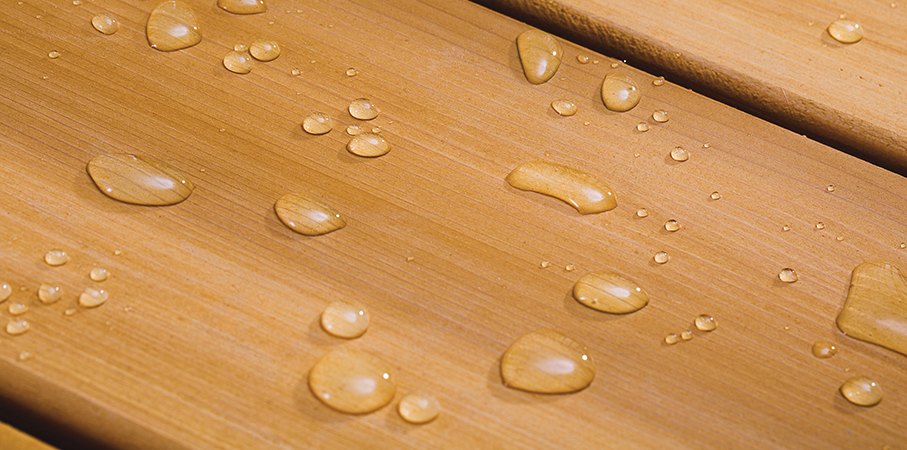 Extreme close-up of stained deck board with water beading. 