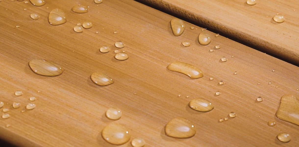 Close-up of a wooden deck with water droplets beading on the surface, showing the effectiveness of Thompson's WaterSeal in waterproofing and protecting the wood.