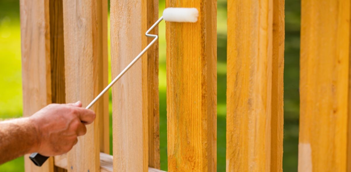 Person using a paint roller to apply Thompson's WaterSeal to a wooden fence, working in small sections to achieve an even and smooth finish.